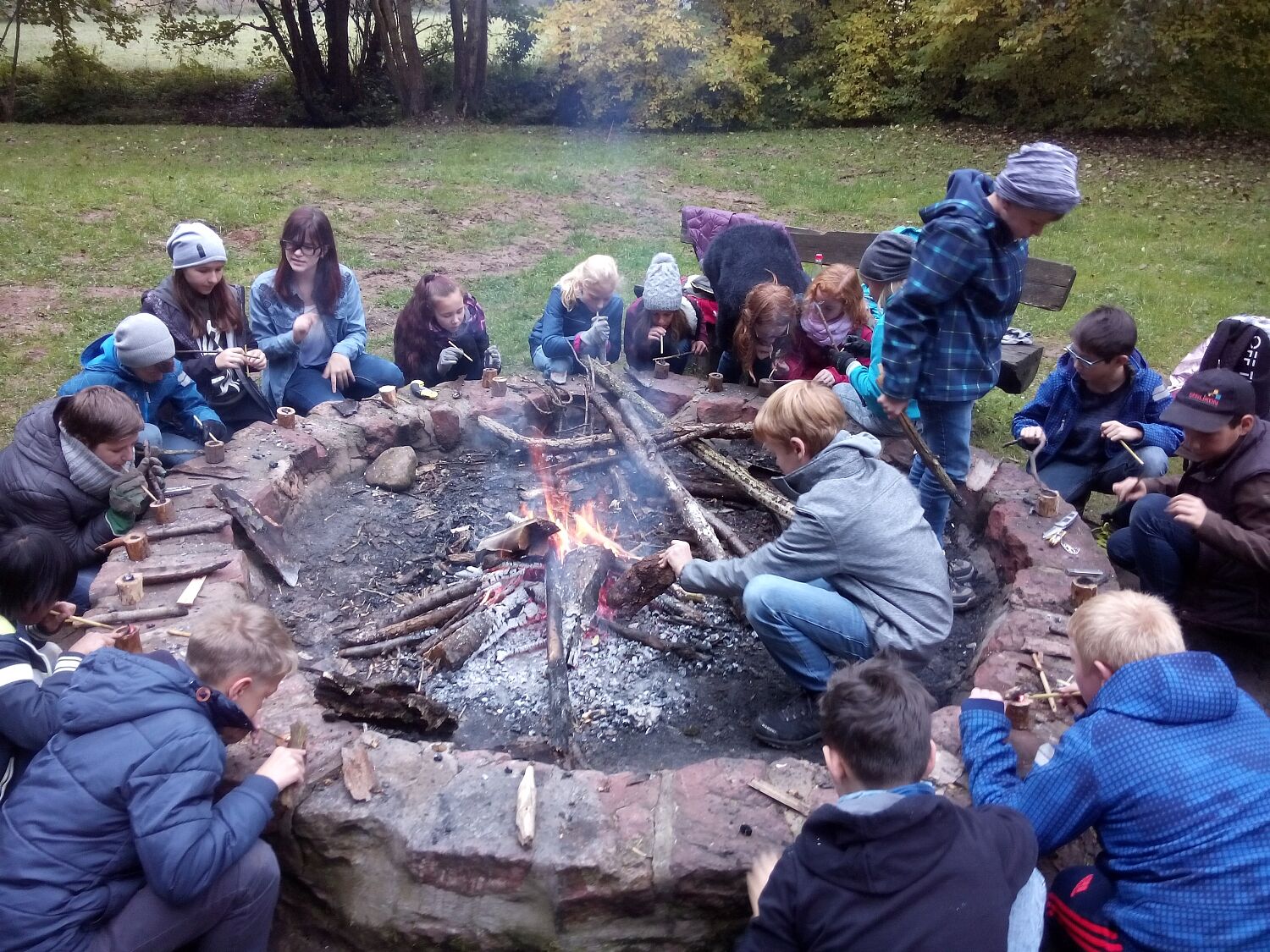 Schüler glühen einen Holzbecher an der Lagerfeuerstelle aus